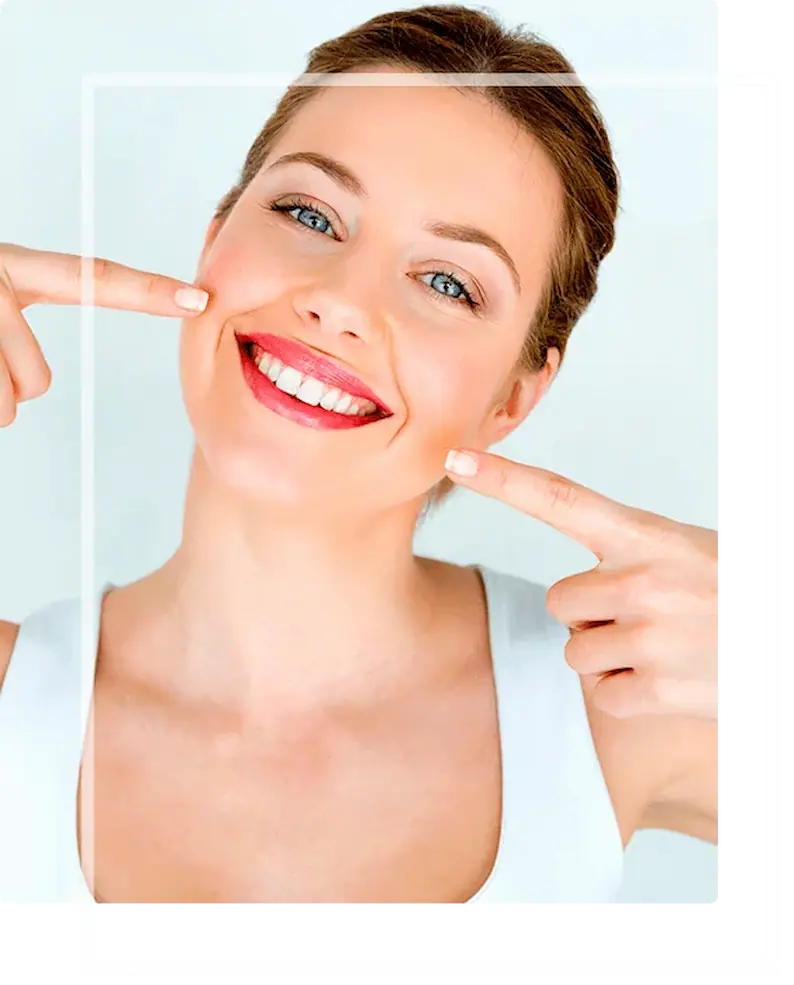 Mulher feliz sorrindo de forma espontânea e apontando para seus dentes brancos e alinhados, simbolizando a conquista da autoestima com a harmonização facial e estética do sorriso na Clínica Cora em Balneário Camboriú.